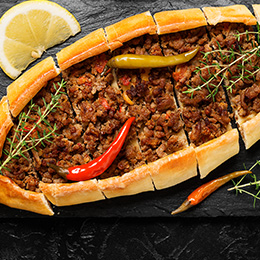 Pide turc en forme de barque, pâte garnie de fromage et viande, plat convivial servi chaud dans les tavernes.